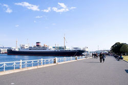 横浜ベイブリッジ港に停泊する巨大船を眺めながら海辺を散歩する人々